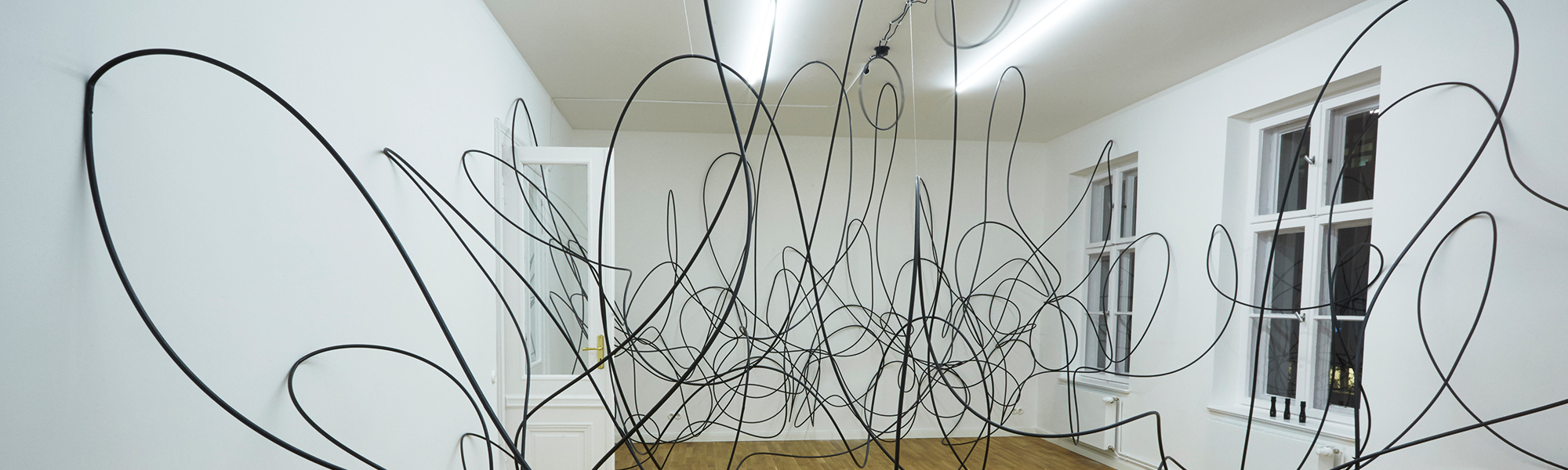 Large Black  Wires Coiled and Spiralling inside a white walled room