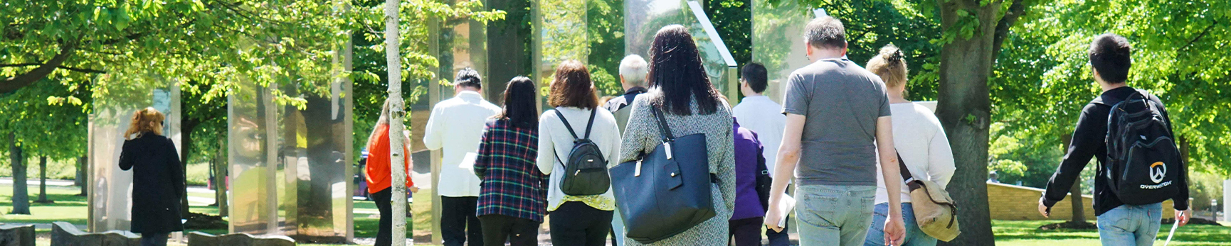 A group of people holding Sculpture Walk maps walking and interacting with outdoor sculptures.