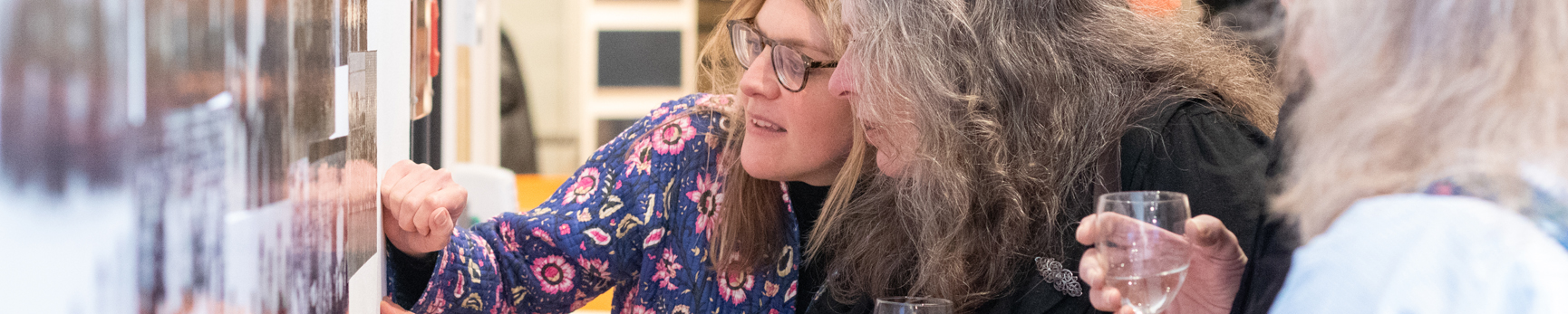 Two women holding glasses of wine while looking at artworks