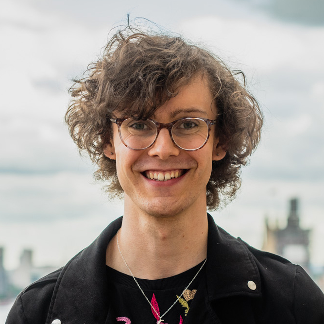 A headshot of person with curly brown hair and glasses