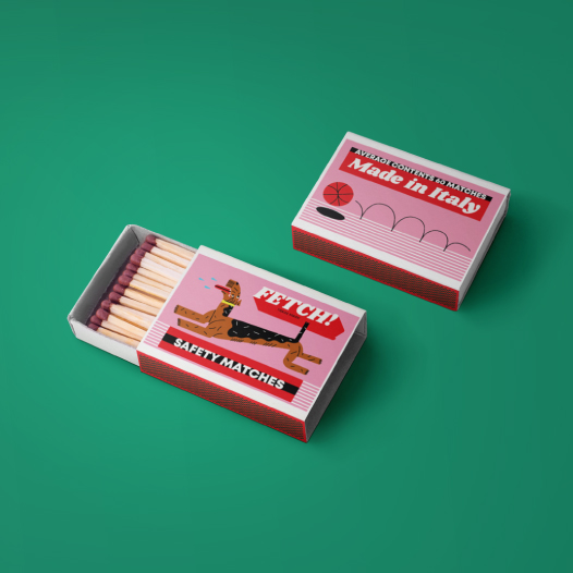 Two bold pink matchboxes on a green background, one matchbox is open and shows a black and brown excited dog on the packaging. The other matchbox is closed and shows an orange basketball bouncing.
