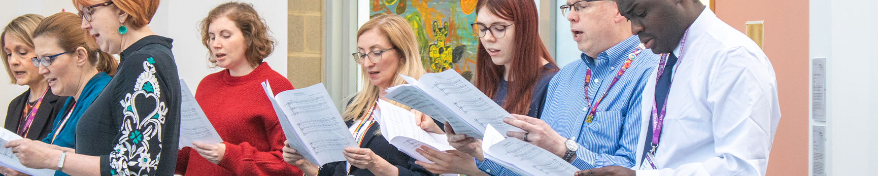 Staff and student choir singing in the gallery, holding sheet music.