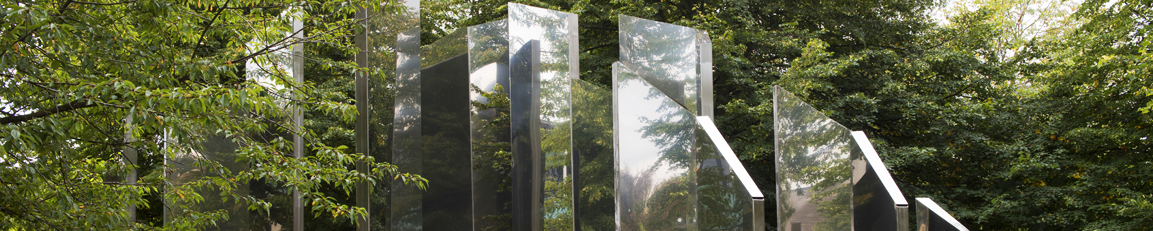 The top of a large steel sculpture surrounded by trees.